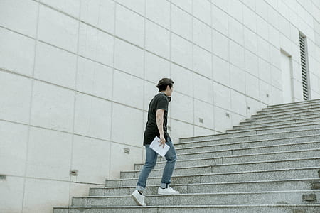 man carrying white book while walking upstairs beside white concrete wall thumbnail