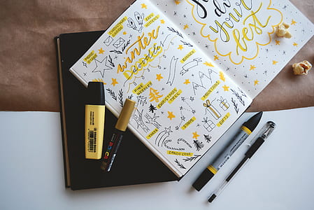 open book with yellow and black writings beside pens and markers thumbnail
