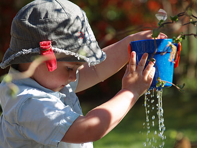 selective focus photo of child holding blue plastic pail toy in gray bucket hat thumbnail