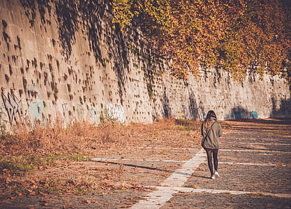 woman walking on gray concrete road beside gray concrete wall thumbnail
