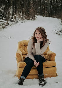 woman sitting on sofa outside surrrounded by trees filled with snow during daytime thumbnail