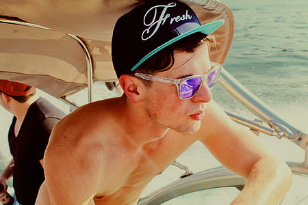 topless man wearing cap and sunglasses riding bowrider during daytime thumbnail
