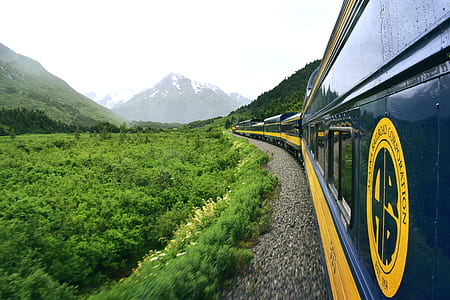 blue and yellow train surrounded by mountains at daytime thumbnail