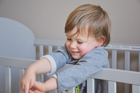 baby wearing gray long-sleeved shirt standing on white wooden crib thumbnail