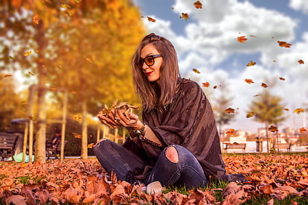 woman wearing black top and distressed jeans sitting on dried leaves thumbnail