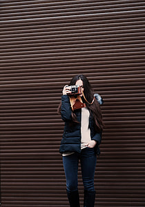 woman holding black camera standing beside brown shutter door thumbnail