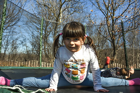girl wearing white long-sleeved shirt splitting her legs on trampoline with enclosure thumbnail