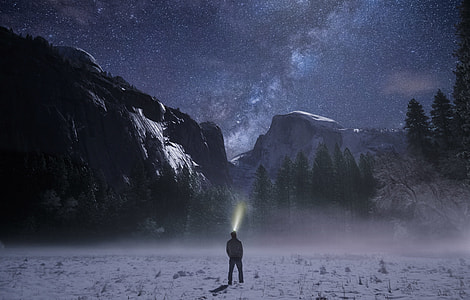 photo of standing man in white jacket facing green trees and grey mountain thumbnail