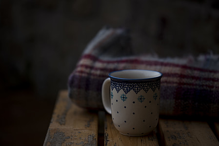 white and blue ceramic mug on brown wooden board near red textile thumbnail