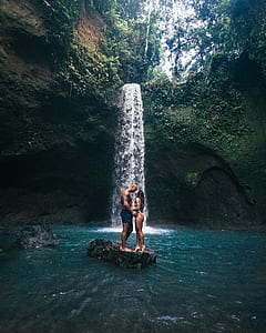 couple standing on rock about to kiss near waterfall during daytime thumbnail