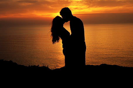 silhouette of man and woman kissing on cliff near body of water during golden hour thumbnail