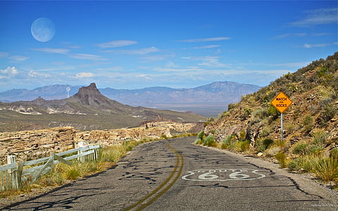 grey empty road between mountains and street side barricade under blue cloudy sky during daytime thumbnail