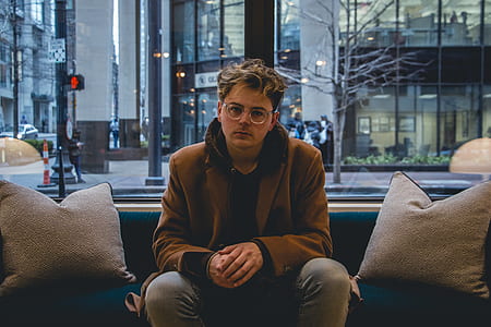 man wearing brown coat sitting on blue sofa thumbnail