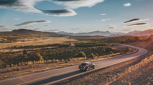 blac vehicle running on road near bushes and mountain during daytime thumbnail