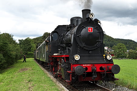 red and black train on gray rail near green grass and green trees under cloudy sky during daytime thumbnail