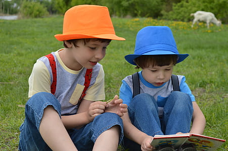 two kids wearing orange and blue fedora hats sitting on grass thumbnail