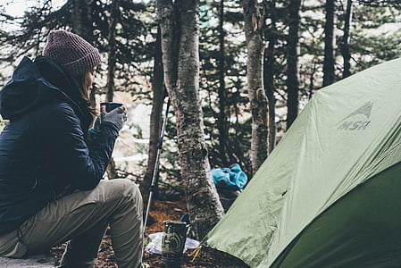woman sitting on rock holding coffee mug beside tent thumbnail