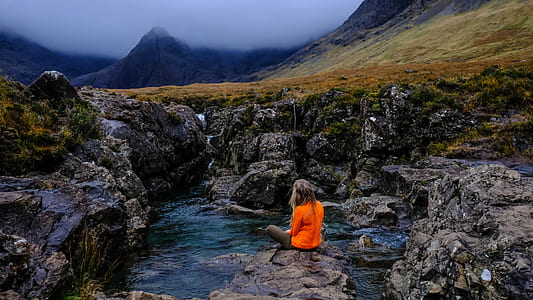 woman sitting on cliff above body of water thumbnail