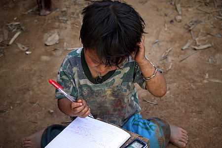 boy holding red pen while looking at white notebook thumbnail