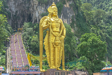 yellow standing Hindu deity statue surrounded by trees during daytime thumbnail