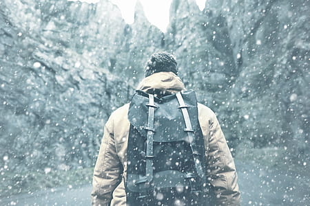 man with black backpack walking near black rock formations thumbnail