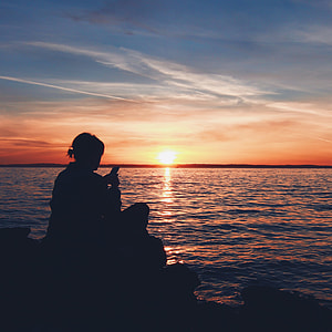 silhouette of person sitting on rock in beach thumbnail