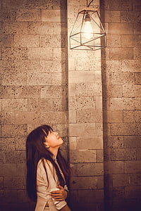 woman looking up a light bulb turned on near wall thumbnail
