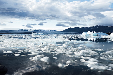 brown mountain covered by snow near icy body of water under white clouds thumbnail
