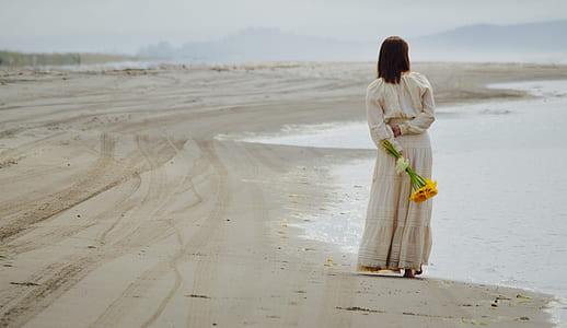 woman holding yellow flowers while standing beside the shore thumbnail