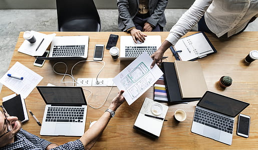 person holding white paper near brown wooden table with several laptop computers thumbnail
