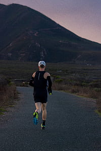 man wearing black top and shorts jogging on concrete road thumbnail