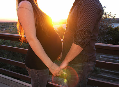pregnant woman holds hand with a man at golden hour time thumbnail