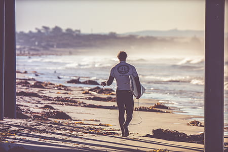 man walking on beach while carrying surfboard thumbnail