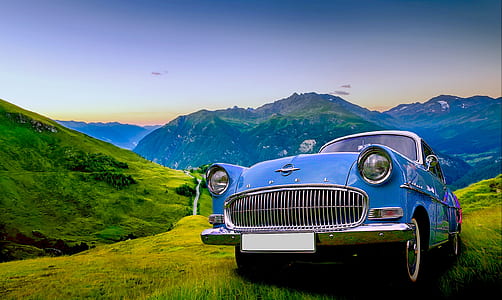 classic blue car parked on green field near hills during daytime thumbnail