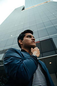 man left hand touching on chin under gray glass building thumbnail