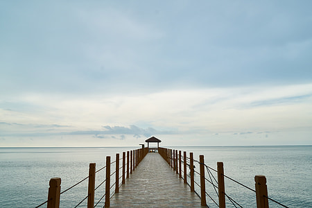 brown wooden dock and gazebo on water under white clouds thumbnail