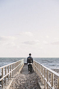 Man in Black Jacket Walking on Gray Concrete Dock thumbnail