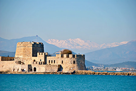 brown concrete building beside body of water overlooking mountains under blue sky at daytime thumbnail