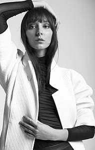 woman wearing white coat standing holding her hair thumbnail