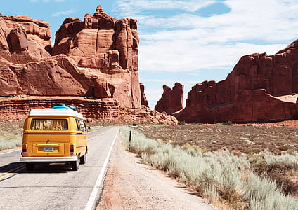 yellow van traveling on concrete road towards red rock monoliths during daytime thumbnail