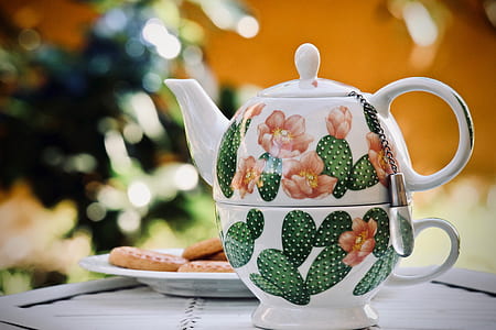 white and green floral teapot near plate of cookies thumbnail