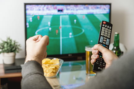 Watching football match on tv with remote controller. thumbnail