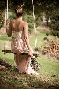 woman wearing pink strapless dress sitting on brown sing during daytime thumbnail
