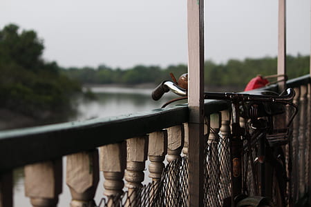 black bicycle beside brown wooden fence near body of water thumbnail