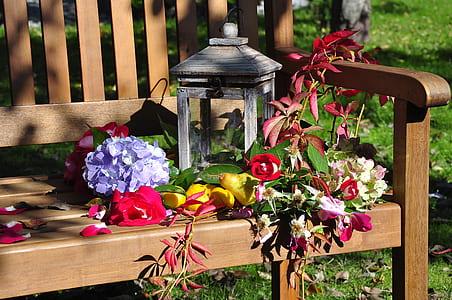 closeup photography of gray candle lantern on bench surrounded with flowers thumbnail