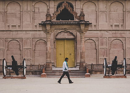 man walking in front of structure beside cannons thumbnail