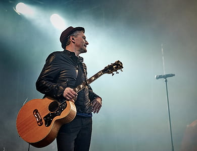 man holding brown dreadnought acoustic guitar at stage thumbnail