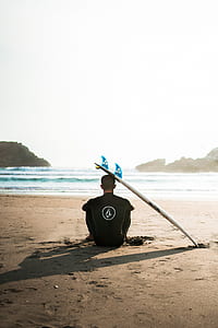 man sitting on sea shore beside surfboard thumbnail