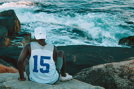 man sitting on brown boulder near sea during daytime thumbnail