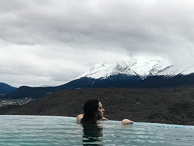 woman swimming in pool facing white mountains thumbnail